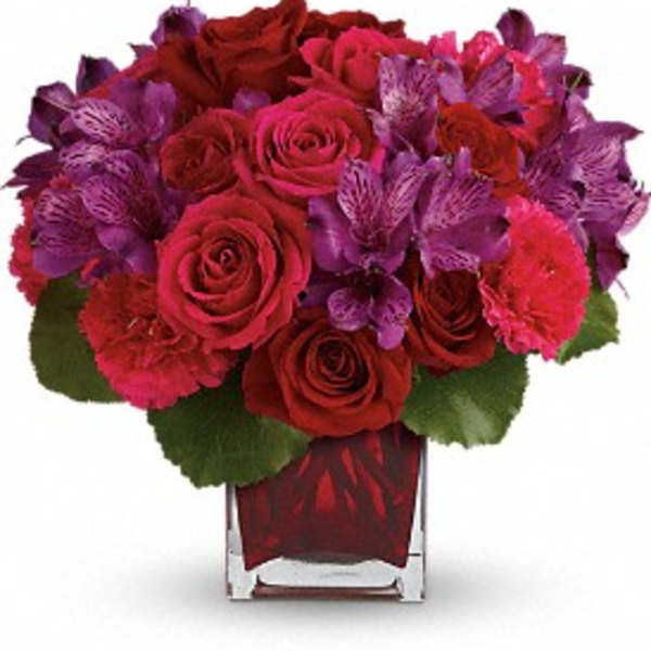Red roses and purple flowers arranged in a clear square vase