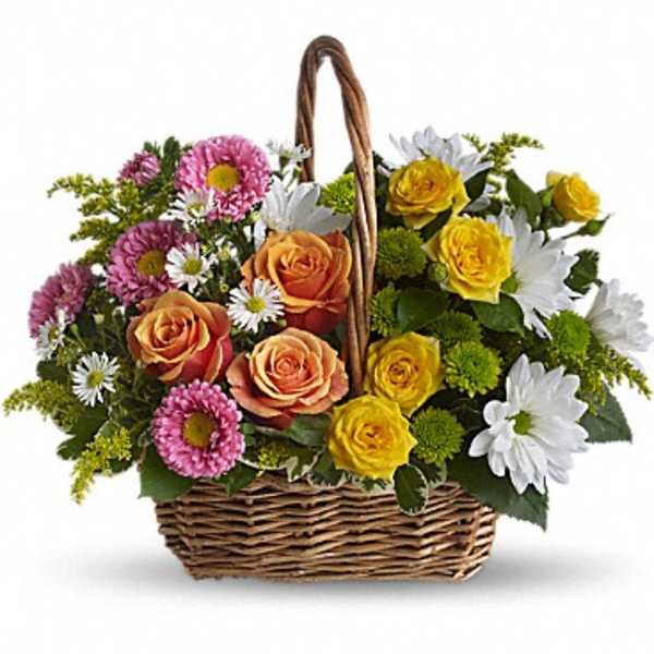 Wicker basket filled with peach and yellow roses, white daisies, and pink blooms in a mixed arrangement