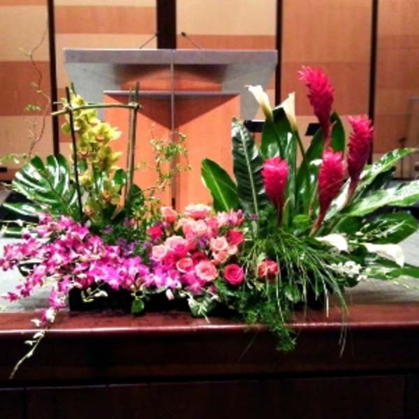 Wide pink and white tropical floral arrangement displayed in front of a wooden podium
