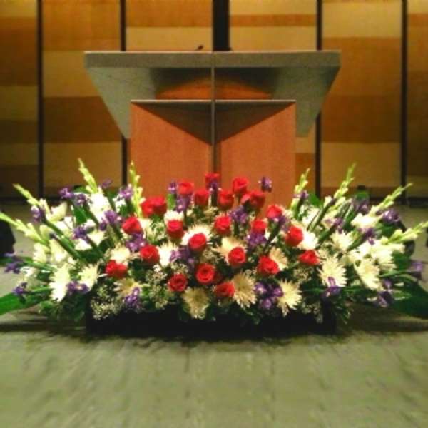 Large red, white, and purple floral spray arranged low in front of a wooden podium.