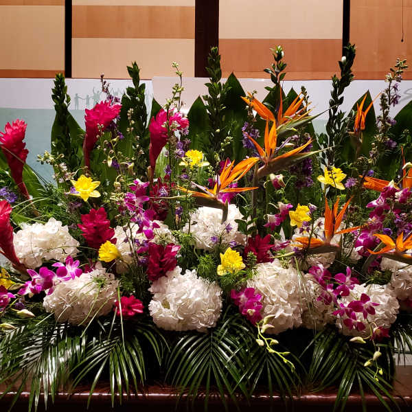Large tropical stage arrangement with white hydrangeas, orange birds of paradise, and bright accent flowers.