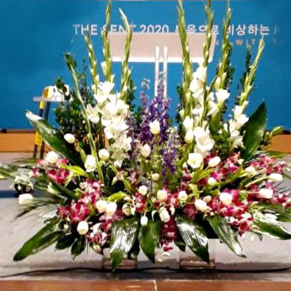 Large stage arrangement with white spikes, purple flowers, and pink orchids in a wide fan shape