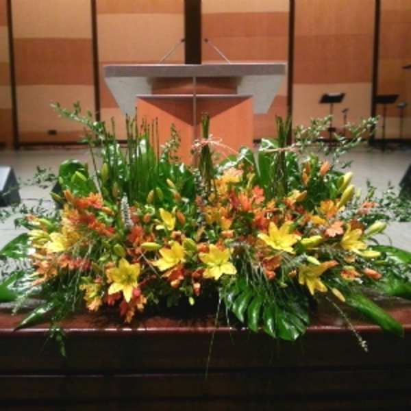 Large yellow and orange floral arrangement with lilies in front of a wooden podium