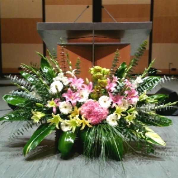 Large stage arrangement of pink lilies, white flowers, and lush greenery in front of a podium