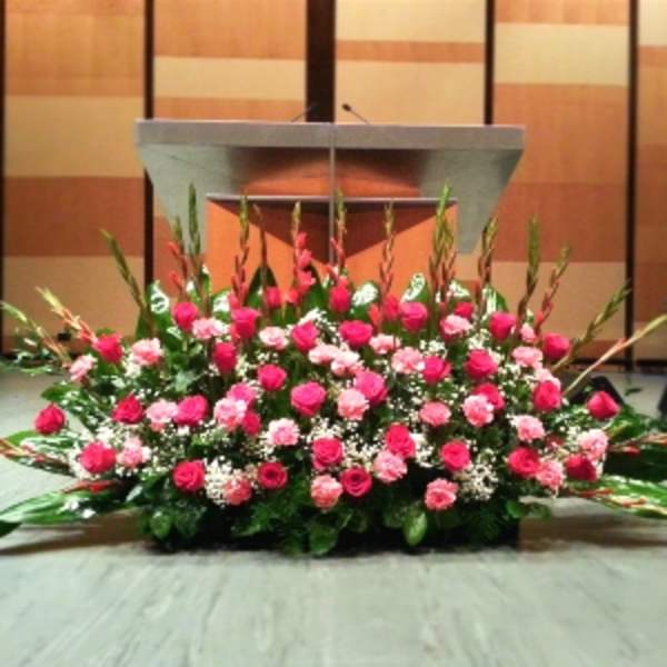 Large pink and white floral stage arrangement with roses and carnations in front of a podium.