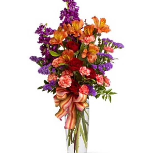Tall mixed bouquet in a clear glass vase with a striped ribbon