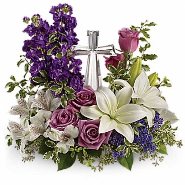 Low arrangement of white lilies and lavender roses with a silver cross in the center