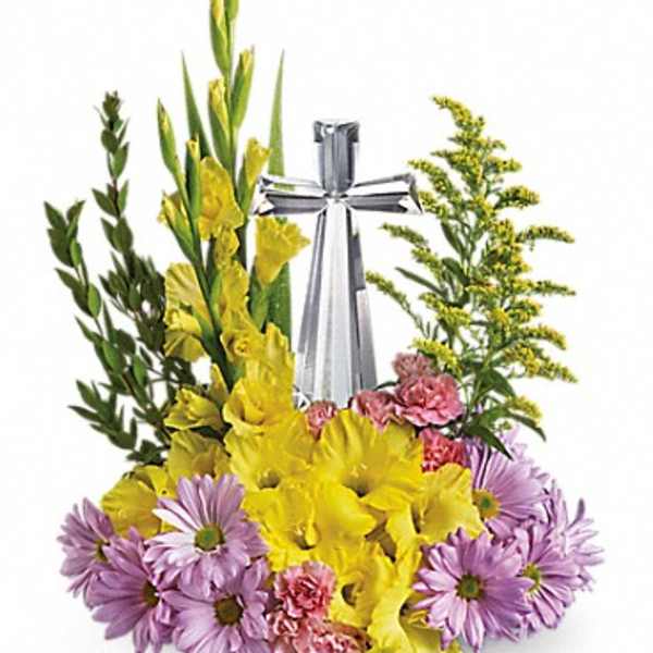 Religious floral arrangement with yellow and lavender blooms surrounding a clear crystal cross.