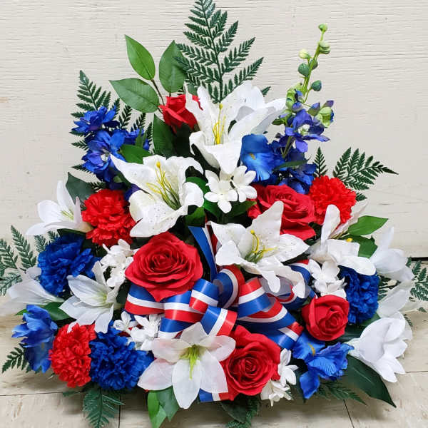 Patriotic arrangement of white lilies, red roses, and blue flowers with a red, white, and blue ribbon