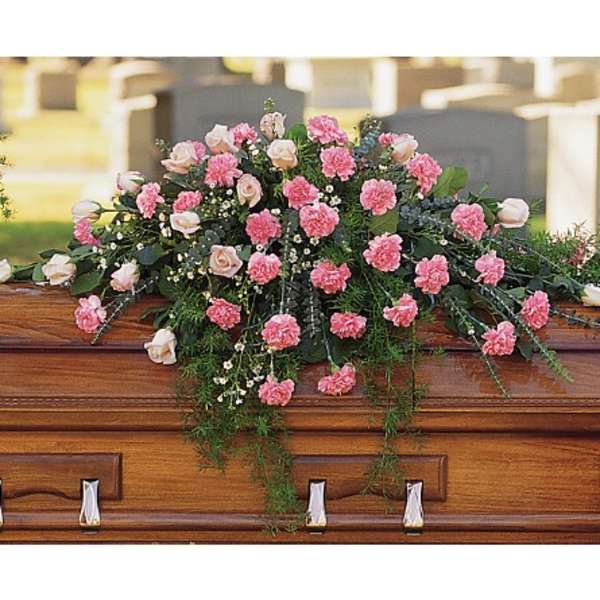 Pink carnations and pale roses arranged as a casket spray on a wooden coffin.