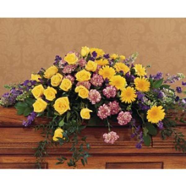 Casket spray of yellow roses, yellow daisies, pink carnations, and purple flowers on a wooden casket