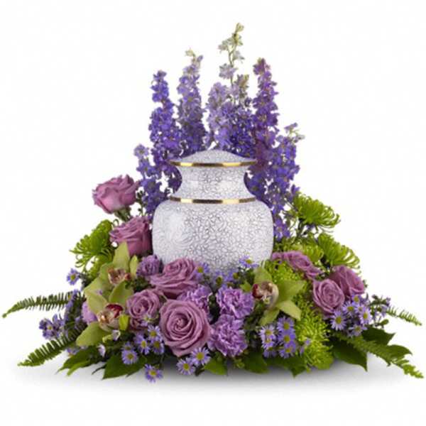 Cremation urn encircled by purple delphinium, lavender roses, and green accent flowers.