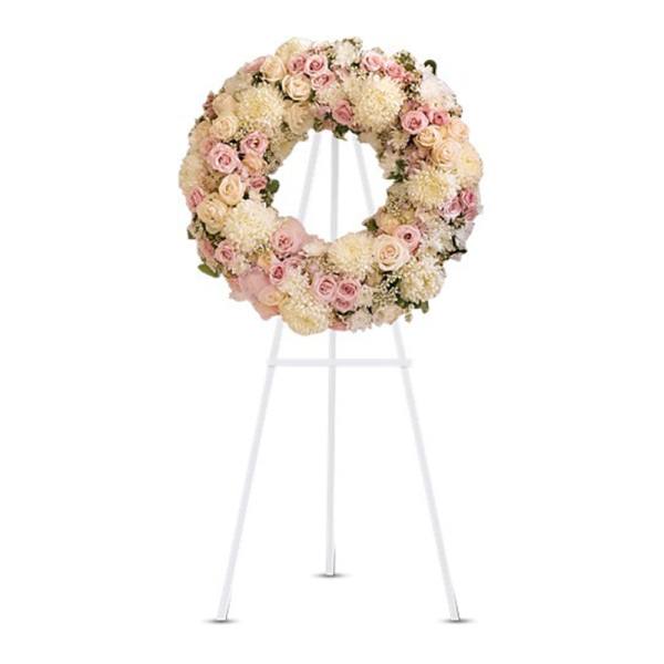 Pale pink and cream floral wreath displayed on a white metal easel.