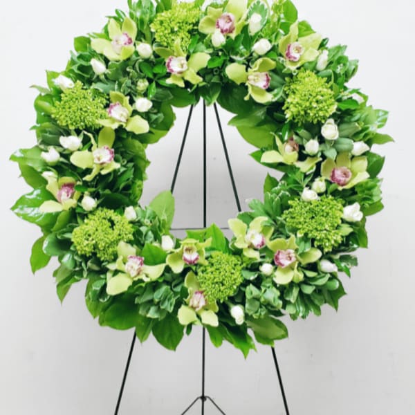 Green floral wreath with orchids and roses displayed on a black metal easel