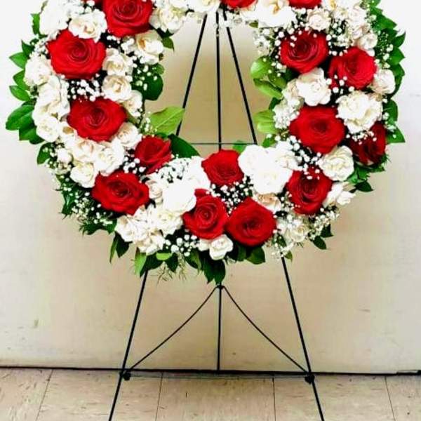 Standing wreath of red and white roses with white filler flowers on a metal easel.