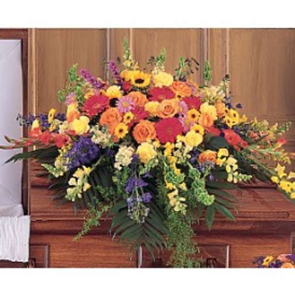 Bright mixed funeral casket spray of yellow, orange, and red flowers on a wooden casket
