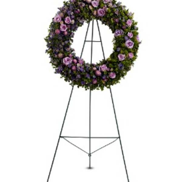Large circular wreath of purple and lavender flowers displayed on a metal stand