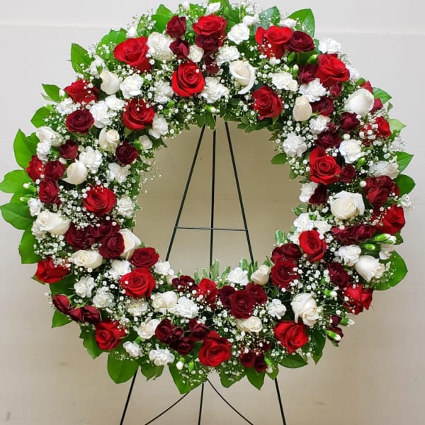 Standing circular wreath of red and white roses and white carnations on a metal easel