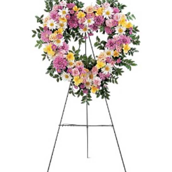 Heart-shaped standing wreath of pink, yellow, and white flowers on a metal easel.
