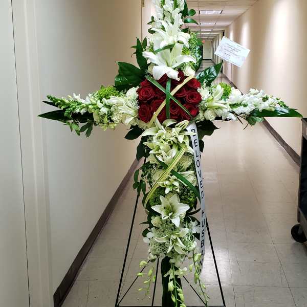 Tall cross-shaped funeral spray with white lilies, snapdragons, and red roses on a metal easel