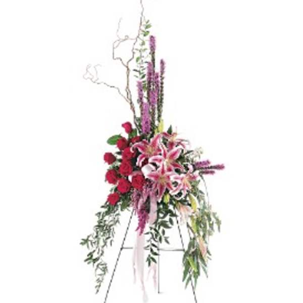 Standing easel spray of pink lilies, red roses, and tall purple spikes with cascading foliage.