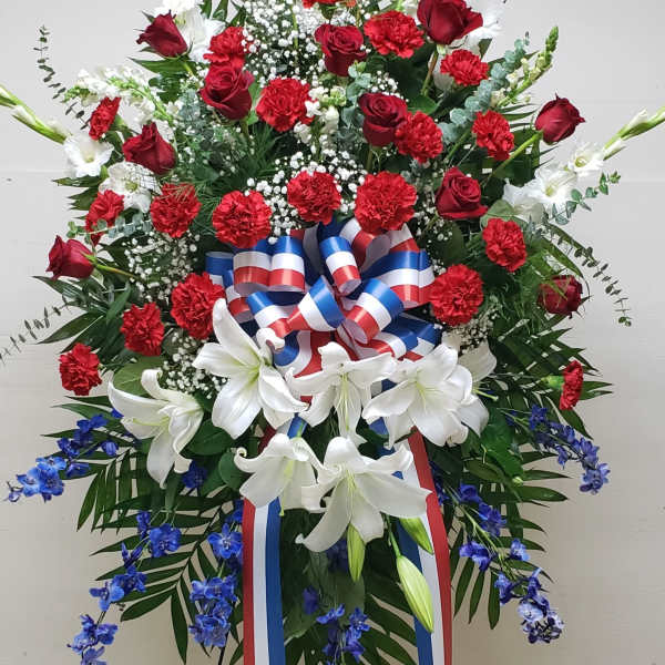 Tall red, white, and blue standing spray with roses, carnations, lilies, and ribbon on an easel
