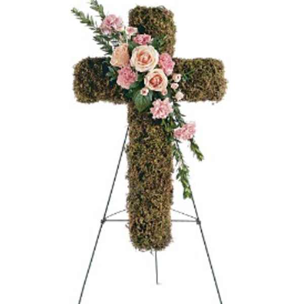 Standing moss-covered cross with pink and peach flowers on a metal easel.