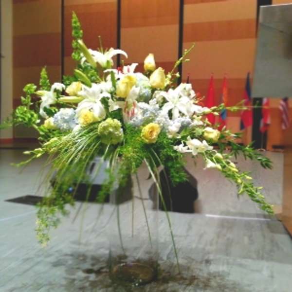 Large white and yellow floral arrangement in a tall stand