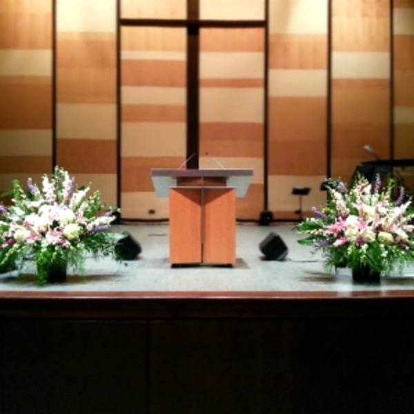 Two large pink, white, and purple altar arrangements flanking a wooden podium on a stage
