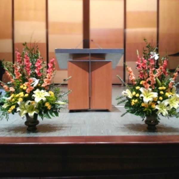 Pair of tall yellow and white lily arrangements with pink blooms on urns flanking a wooden podium