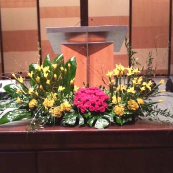 Large altar arrangement of yellow flowers with a central cluster of pink roses before a wooden podium