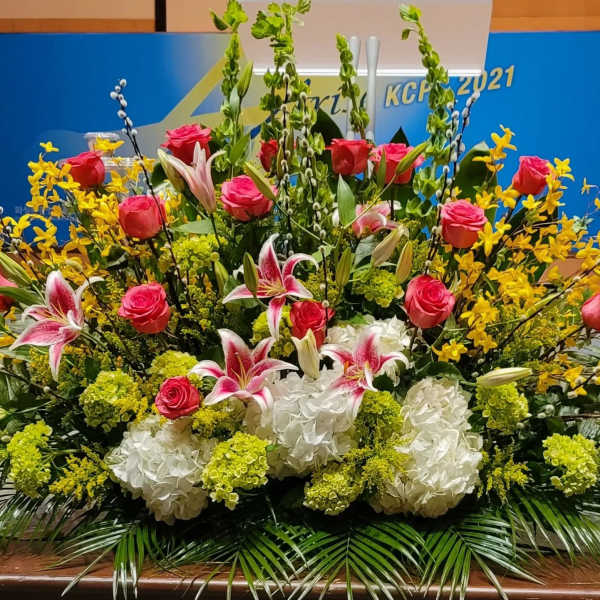 Large stage floral arrangement with pink roses, stargazer lilies, white hydrangeas and yellow flowers