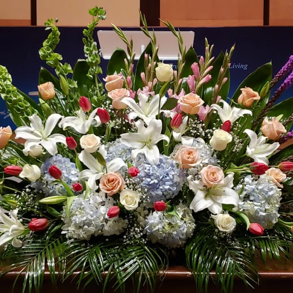 Large front-facing arrangement of white lilies, peach roses, blue hydrangeas, and pink tulips