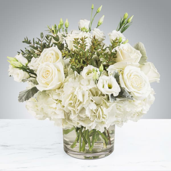 Low arrangement of white roses, hydrangeas, and lisianthus in a clear glass vase