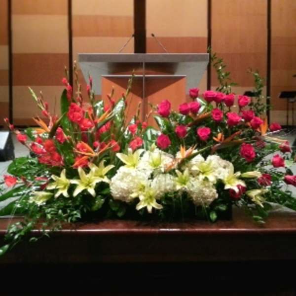 Large altar floral arrangement with pink roses, white hydrangeas, lilies, and tropical blooms.