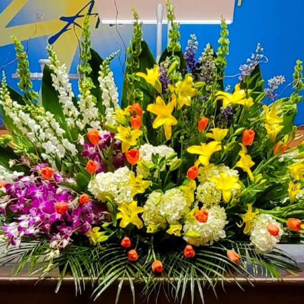 Large mixed arrangement of yellow lilies, white hydrangeas, orange tulips, and purple orchids on a table