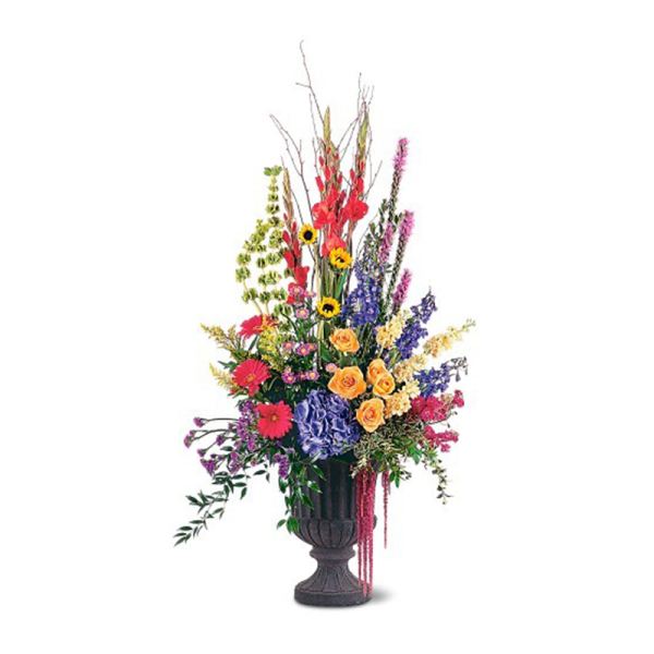 Tall mixed flower arrangement in a dark pedestal urn with bright red, yellow, purple and pink blooms