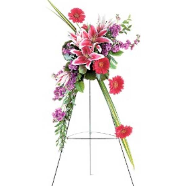Tall standing spray of pink lilies, red gerbera daisies, and purple flowers on a metal easel