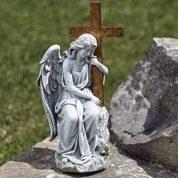 Angel statue seated beside a wooden cross in a cemetery setting