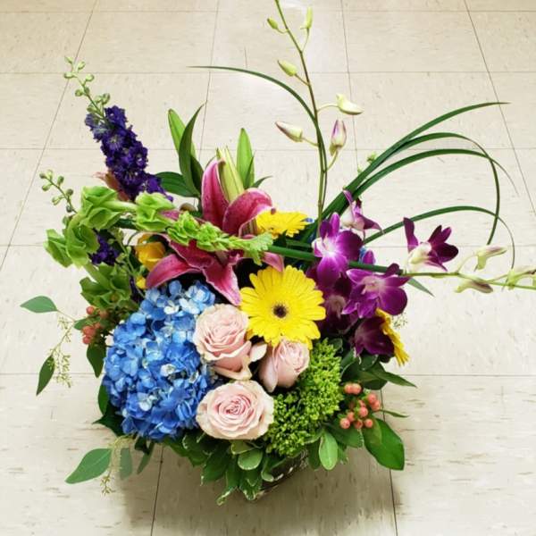 Mixed arrangement of roses, lilies, orchids, gerbera daisies, and hydrangea in a clear glass vase