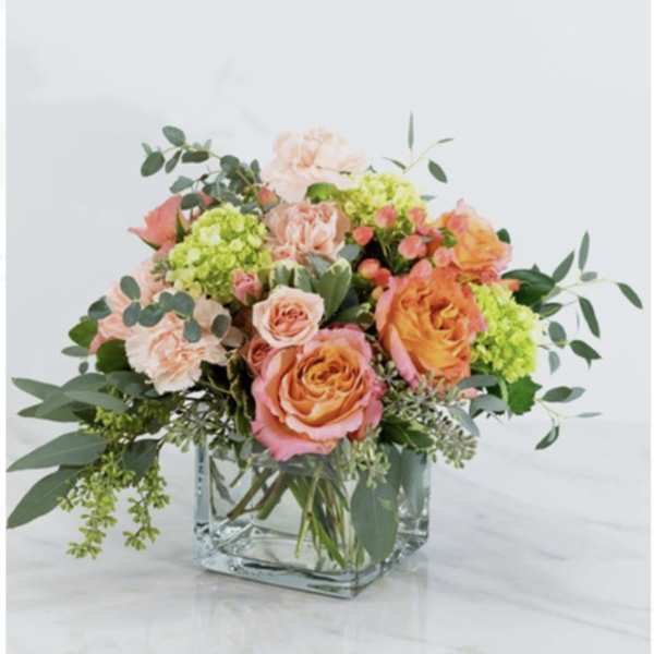 Peach and orange roses with green hydrangeas in a square glass vase
