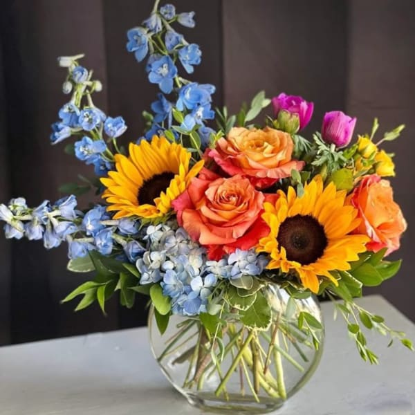 Colorful bouquet with sunflowers, roses, and blue delphinium in a glass vase
