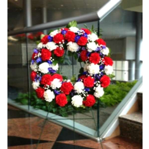 Patriotic wreath of red, white, and blue flowers displayed on a metal easel stand.
