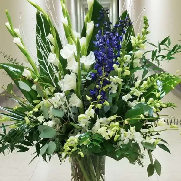 Tall floral arrangement in a clear glass vase with white and blue blooms