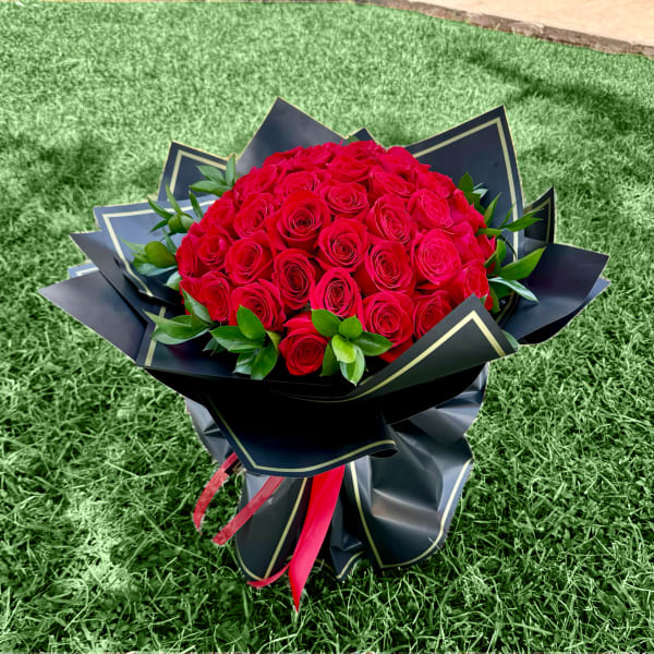 Large bouquet of red roses wrapped in black paper with a red ribbon