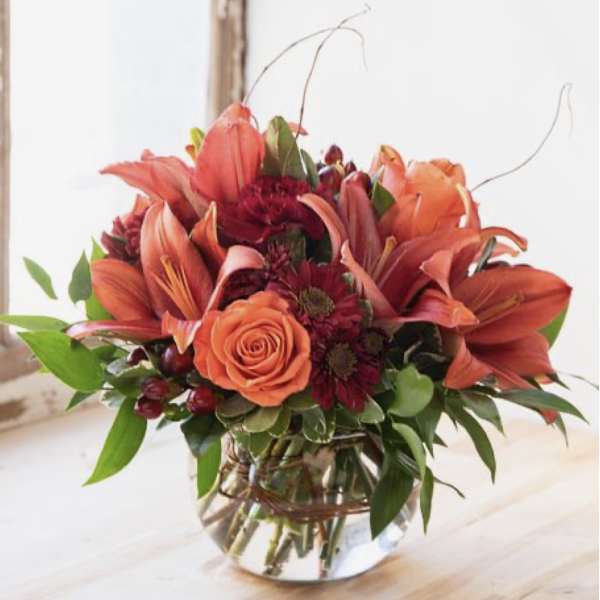 Orange lilies and roses in a clear glass vase