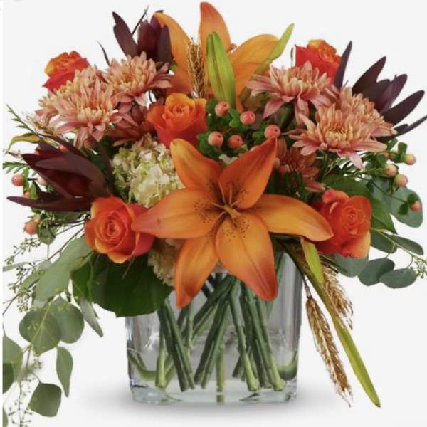 Orange lilies and roses arranged in a clear glass vase