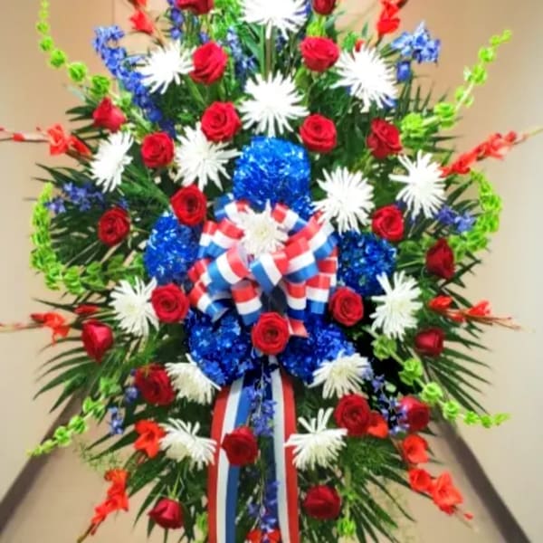 Patriotic standing spray of red roses, white mums, and blue accents with striped bow on an easel