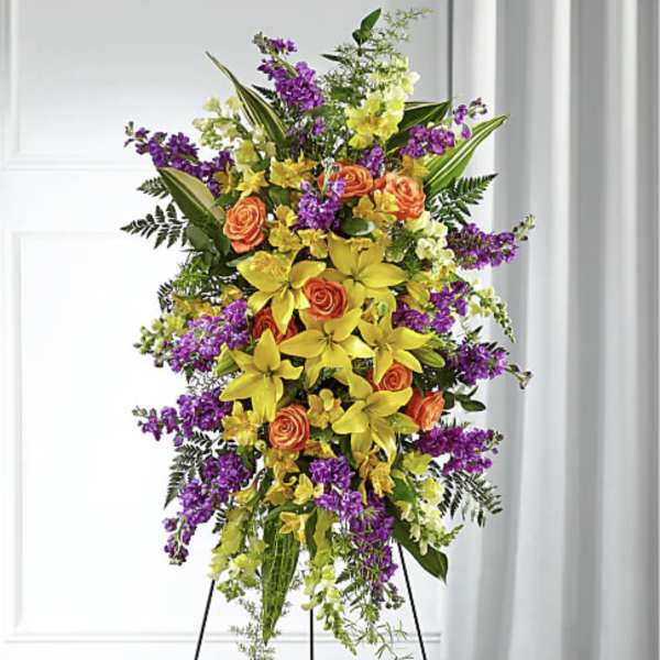 Tall standing floral spray with yellow lilies, orange roses, and purple blooms