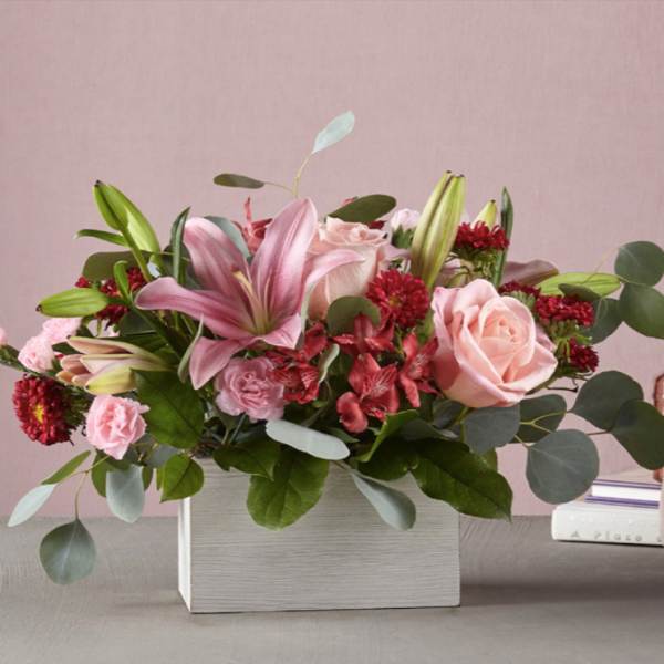 Pink lilies and roses arranged in a white box with greenery